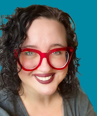 A portrait of Erin, a smiling white woman with curly brown hair, and wearing red glasses.