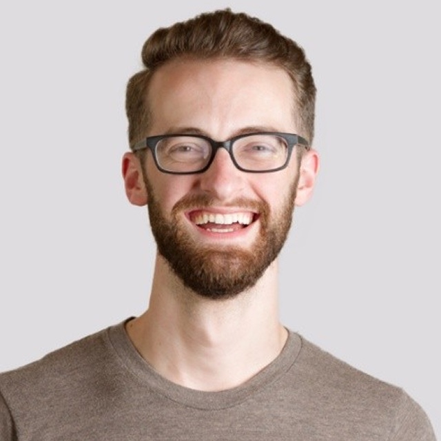 A portrait of Jake Buob, a smiling white man with brown hair, a brown beard, and wearing glasses.