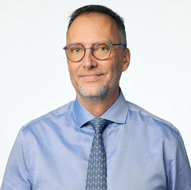 Headshot photo of John Vasko, a gently smiling white man wearing glasses and a shirt and tie.